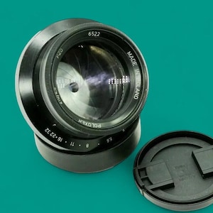 Può includere: Un obiettivo per fotocamera nero con la scritta "POLOXER" e "MADE IN POLAND". L'obiettivo presenta una serie di numeri e marcature, tra cui "8", "11", "16", "22" e "32". Un tappo nero per l'obiettivo è accanto all'obiettivo.