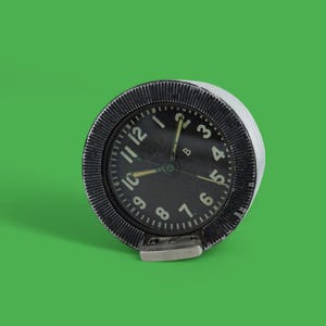 May include: A black and silver round clock face with white numbers and hands. The clock face is surrounded by a silver ring with a black outer ring.