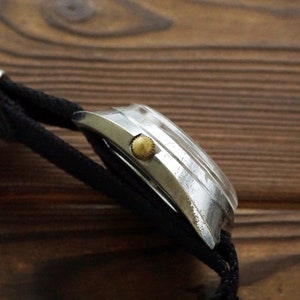 Pode incluir: Um rel&oacute;gio de pulso prateado com uma pulseira de nylon preta. O rel&oacute;gio tem uma coroa dourada e uma caixa prateada.