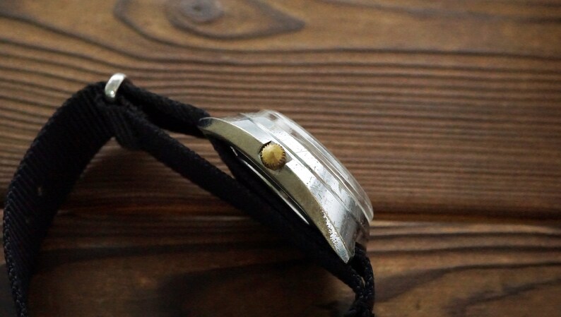 Pode incluir: Um rel&oacute;gio de pulso prateado com uma pulseira de nylon preta. O rel&oacute;gio tem uma coroa dourada e uma caixa prateada.