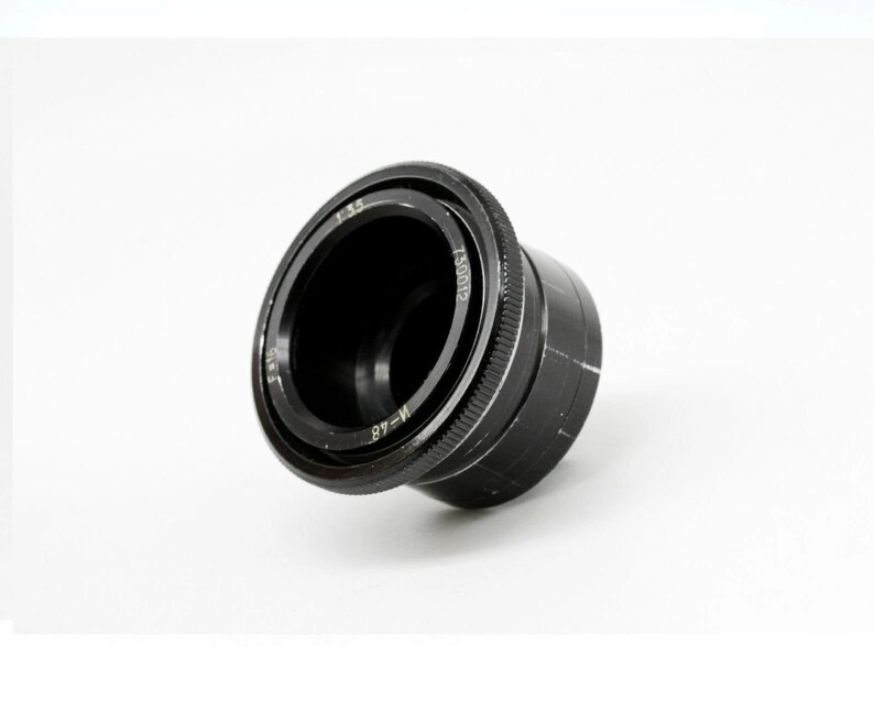 K&ouml;nnte beinhalten: Ein schwarzes Kameraobjektiv mit den Markierungen "f 3.5" und "M-48". Das Objektiv hat einen geriffelten Fokusring und befindet sich vor einem wei&szlig;en Hintergrund. Es ist ein Fotozubeh&ouml;r.