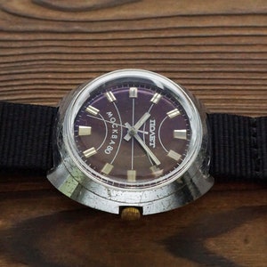 Pode incluir: Um rel&oacute;gio de pulso prateado com uma pulseira de nylon preta. O mostrador do rel&oacute;gio &eacute; roxo escuro com ponteiros e marcadores prateados. O mostrador do rel&oacute;gio tamb&eacute;m tem o texto "МОСКВА" e "СССР" impresso nele.