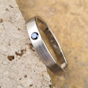 Peut inclure: Une bague simple en argent avec un seul diamant noir serti au centre.