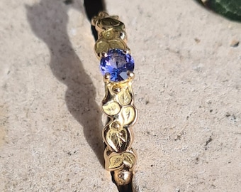 May include: A gold ring with a purple gemstone set in the center. The ring is decorated with a floral design.