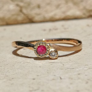 Peut inclure: Une délicate bague en or avec une pierre précieuse en rubis rouge sertie dans une bélière perlée et un petit accent en diamant.