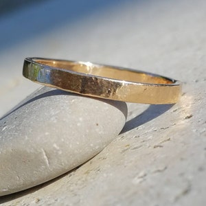 Peut inclure: Une simple bague en or avec une finition martelée. La bague repose sur une pierre lisse et grise.