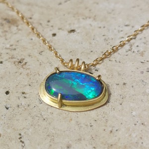 Peut inclure: Un collier en or avec un pendentif en forme d'opale ovale de grande taille aux couleurs irisées vertes, bleues et noires.