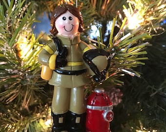 Può includere: Un ornamento natalizio in ceramica che raffigura un pompiere con un casco marrone, una giacca gialla e stivali neri. L'ornamento tiene un tubo antincendio e un idrante.