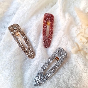 Puede incluir: Tres pinzas para el pelo brillantes en plata, oro y rosa. Las pinzas son rectangulares y tienen un acabado brillante.