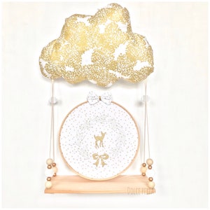 Peut inclure: Un nuage dor&eacute; &agrave; paillettes avec un n&oelig;ud blanc est suspendu au-dessus d'un cercle blanc et dor&eacute; avec un motif de cerf dor&eacute; &agrave; paillettes et de couronne. Le cercle est sur une &eacute;tag&egrave;re en bois avec des perles dor&eacute;es et blanches suspendues sur les c&ocirc;t&eacute;s. Le texte "DOLCE PERLA" est sur l'&eacute;tag&egrave;re.