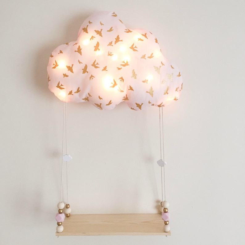 Peut inclure: Une veilleuse en forme de nuage rose avec des accents d'oiseaux dor&eacute;s est suspendue &agrave; une &eacute;tag&egrave;re en bois avec des perles blanches et roses. Le nuage est &eacute;clair&eacute; par des lumi&egrave;res LED blanc chaud.