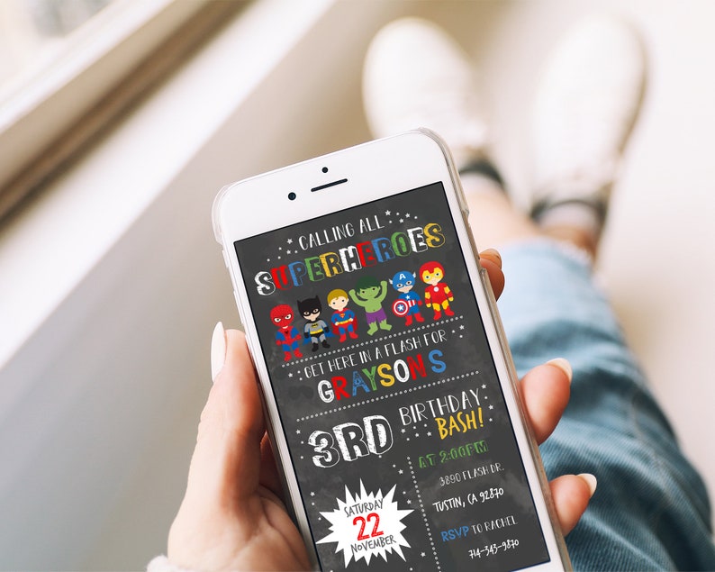 May include: A superhero-themed birthday party invitation with a chalkboard background. The invitation features a group of cartoon superheroes, the text "Calling all Superheroes", and the details of the party, including the date, time, and location. The invitation is displayed on a smartphone.