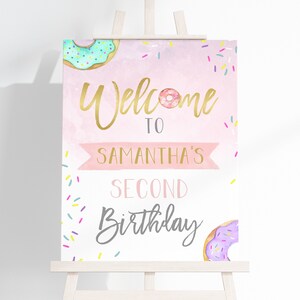 May include: Welcome to Samantha's Second Birthday sign with a pink background, gold lettering, and donut illustrations. The sign is decorated with colorful sprinkles.