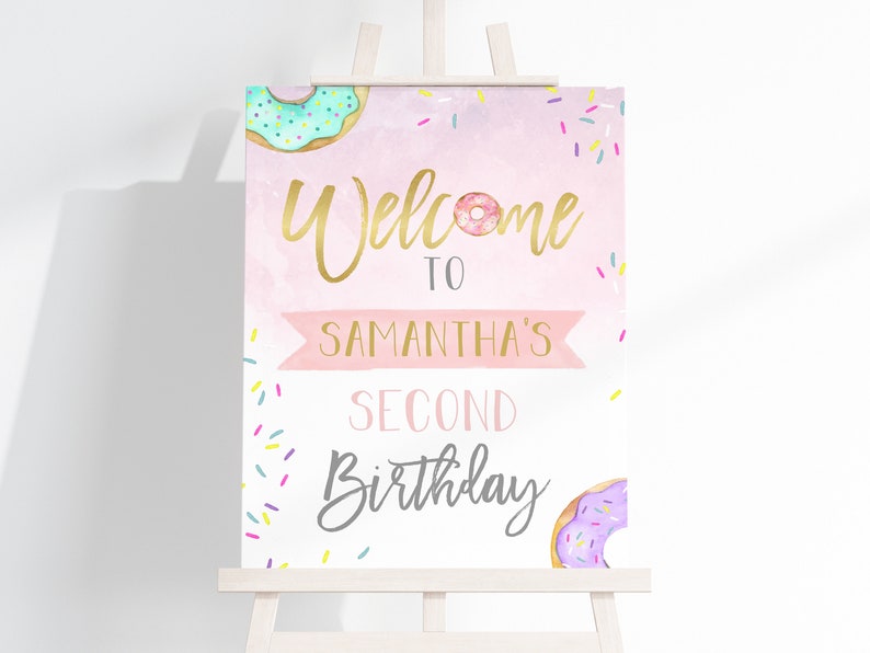 May include: Welcome to Samantha's Second Birthday sign with a pink background, gold lettering, and donut illustrations. The sign is decorated with colorful sprinkles.