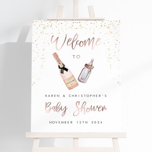 Puede incluir: Un letrero de bienvenida para un baby shower en un caballete blanco. El letrero presenta texto e ilustraciones en oro rosa de una botella de champ&aacute;n y un biber&oacute;n. El texto dice "Bienvenida a la fiesta de bienvenida de Karen y Christopher el 15 de noviembre de 2024."