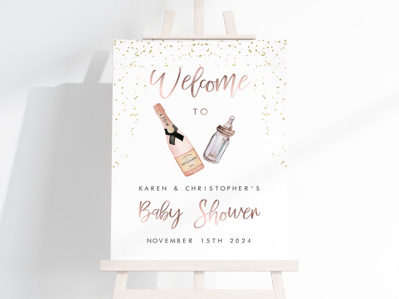 Puede incluir: Un letrero de bienvenida para un baby shower en un caballete blanco. El letrero presenta texto e ilustraciones en oro rosa de una botella de champ&aacute;n y un biber&oacute;n. El texto dice "Bienvenida a la fiesta de bienvenida de Karen y Christopher el 15 de noviembre de 2024."