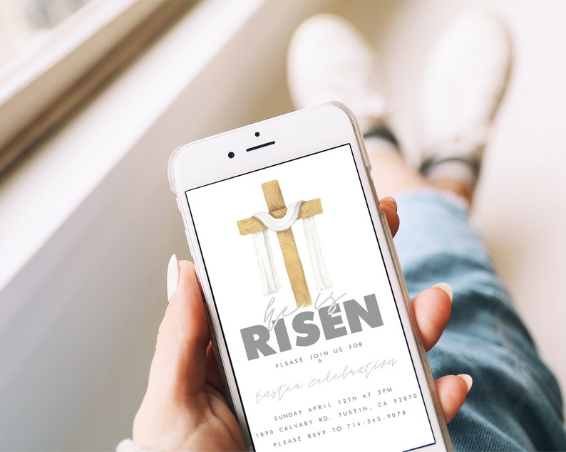 May include: A smartphone displaying a digital invitation for an Easter celebration. The invitation features a watercolor illustration of a wooden cross with a white cloth draped over it. The text reads "He is Risen" in gray lettering. The invitation includes the date, time, and location of the event, as well as an RSVP number.