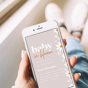 May include: A mobile phone screen displaying a baby shower invitation with a light pink background and white daisies. The invitation reads "baby in bloom" in white and orange text. The text also includes the name "Renee Reynolds", the date and time of the shower, and the address.