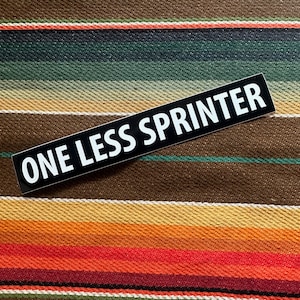 Może przedstawiać: Czarno-biała naklejka z tekstem "ONE LESS SPRINTER" na kolorowym, paskowanym tle.
