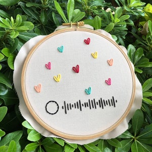 May include: Embroidered hoop art with a black and white barcode and colorful hearts in shades of pink, red, yellow, blue, and orange.