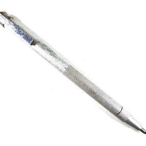 May include: A silver metal mechanical pencil with a textured grip. The pencil has a clip and a pointed tip. The body of the pencil is silver and shows signs of wear. The pencil is designed for writing or drawing.