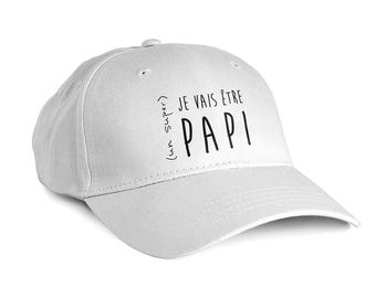 Peut inclure: Une casquette de baseball blanche avec le texte noir imprimé sur le devant. Le texte indique "(un super) JE VAIS ÊTRE PAPI" dans une police sans empattement. La casquette présente une calotte structurée, une visière courbée et des œillets.