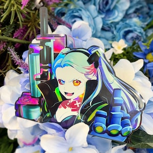 Può includere: Adesivo olografico raffigurante un personaggio in stile anime con capelli turchese e rosa e occhi diversi. Il personaggio indossa un abito nero con una croce rossa. Lo sfondo è composto da fiori blu e bianchi.