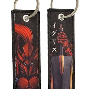 Puede incluir: Dos llaveros negros con herrajes de metal plateado. Cada llavero tiene una etiqueta rectangular con un diseño único. Uno presenta un guerrero rojo, el otro una espada y texto japonés. La parte inferior de la segunda etiqueta dice "MODIFIED DECALS".