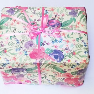Puede incluir: Una caja de regalo envuelta en papel con estampado floral y una cinta rosa atada en un lazo.