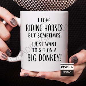 May include: White ceramic coffee mug with black text that reads "I love riding horses but sometimes I just want to sit on a big donkey!"  The text "RISK - A DESIGNS" is printed in black at the bottom of the mug.