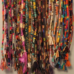 May include: A collection of colourful, multi-stranded hair extensions with various beads and charms. The extensions are hanging from a metal rack.