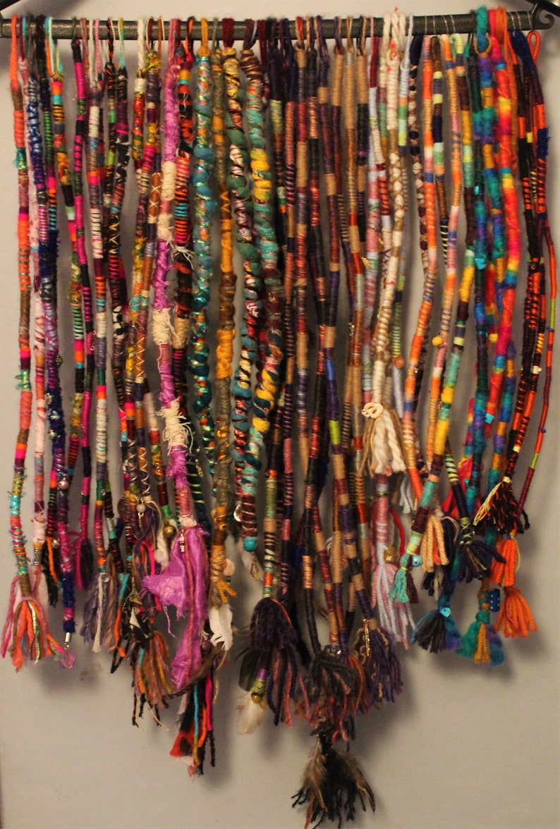 May include: A collection of colourful, multi-stranded hair extensions with various beads and charms. The extensions are hanging from a metal rack.