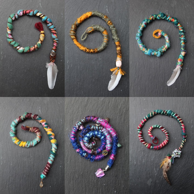 May include: Six colourful crocheted hair wraps with feathers and beads. The wraps are made of different colours and patterns, including blue, green, red, yellow, and purple.