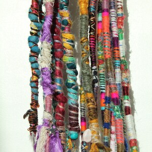 May include: A collection of colourful, multi-coloured, and patterned synthetic hair extensions. The extensions are tied together at the top and hang down in a variety of lengths. Some extensions have beads, feathers, and other decorative elements.