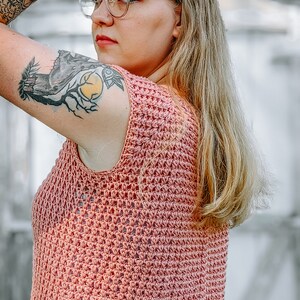 Puede incluir: Un top de ganchillo sin mangas de color coral. El top tiene un diseño texturizado de tejido abierto. La persona lleva gafas con montura dorada. La persona tiene el pelo largo y rubio y tatuajes en el brazo.