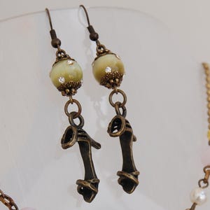 Può includere: Una collana a catena dorata con perline rosa e bianche e una perla verde a forma di occhio. Orecchini abbinati con perline verdi a forma di occhio e ciondoli a forma di scarpa in bronzo.