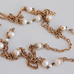 Puede incluir: Un collar de cadena dorada con detalles de perlas blancas. La cadena est&aacute; en capas y presenta detalles intrincados.