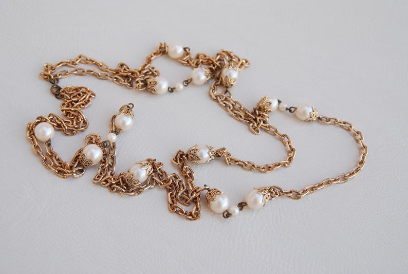 Puede incluir: Un collar de cadena dorada con detalles de perlas blancas. La cadena est&aacute; en capas y presenta detalles intrincados.