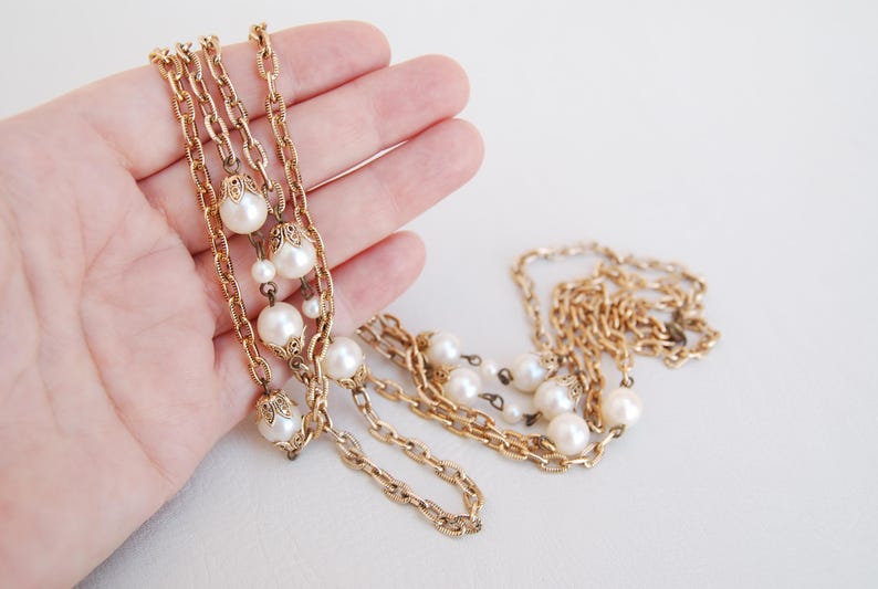Puede incluir: Un collar de cadena dorada con m&uacute;ltiples hebras y detalles de perlas. El collar est&aacute; en capas y presenta un dise&ntilde;o de cadena delicado.