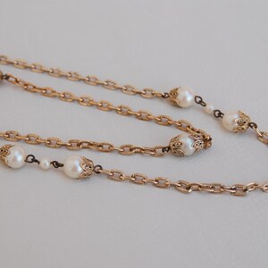 Puede incluir: Un collar de cadena dorada con detalles de perlas. El collar tiene una cadena delicada y presenta detalles de oro ornamentados alrededor de cada perla.