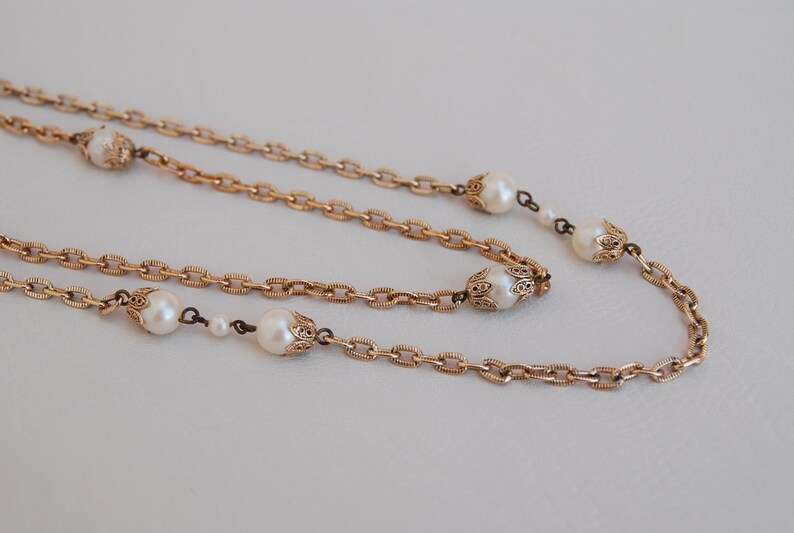Puede incluir: Un collar de cadena dorada con detalles de perlas. El collar tiene una cadena delicada y presenta detalles de oro ornamentados alrededor de cada perla.