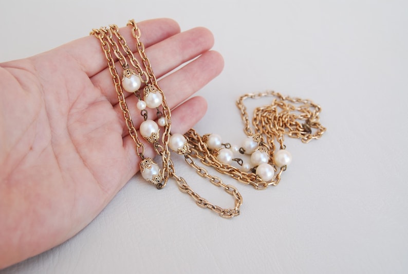 Puede incluir: Un collar de cadena dorada con m&uacute;ltiples hebras y detalles de perlas falsas.