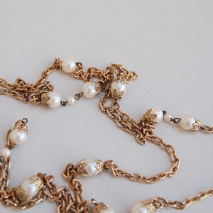 Puede incluir: Un collar de cadena dorada con cuentas de perlas blancas. La cadena est&aacute; hecha de m&uacute;ltiples hebras y tiene un dise&ntilde;o delicado e intrincado.