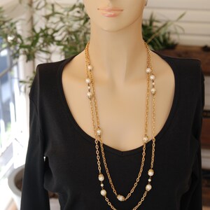 Puede incluir: Una mujer con un top negro y un collar de cadena dorada con detalles de perlas blancas.