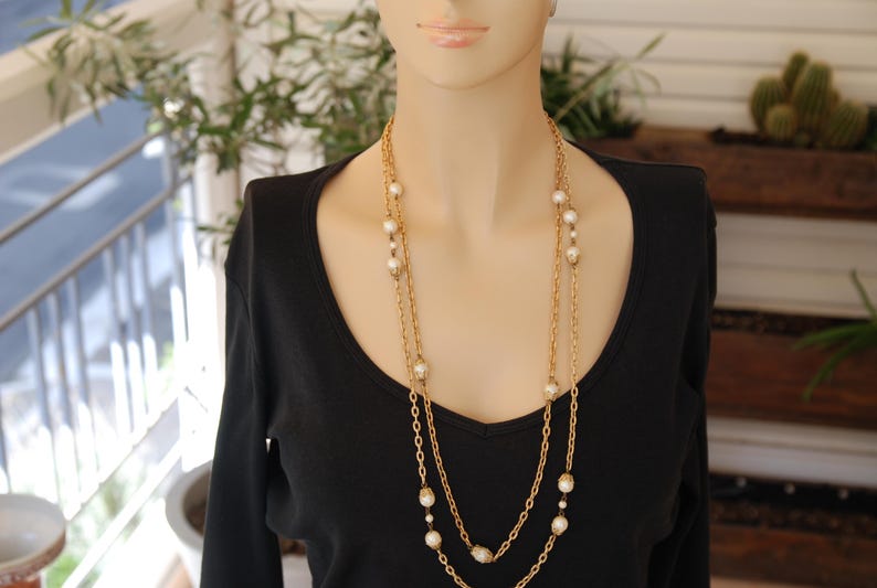 Puede incluir: Una mujer con un top negro y un collar de cadena dorada con detalles de perlas blancas.