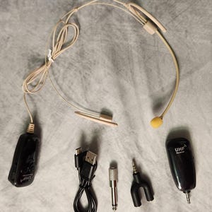 May include: A beige wireless headset microphone with a yellow microphone head, along with a black receiver and transmitter. Also included are a USB charging cable, a metal adapter, and a black audio splitter. The transmitter and receiver have "UHF" printed on them.