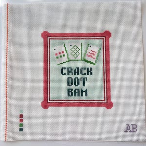 Op de afbeelding: Een wit borduurcanvas met een rode rand en de tekst "CRACK DOT BAM" in zwart. Het ontwerp bevat drie kleine, gestileerde afbeeldingen boven de tekst, met de initialen "AB" in de rechter benedenhoek.