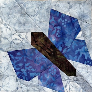 May include: A blue and purple butterfly quilt block with a brown center. The butterfly is made of fabric with a floral pattern.
