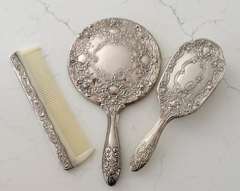 Juego de tocador antiguo de plata con espejo de mano, cepillo y peine.