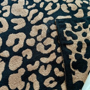 May include: A black and beige throw blanket with a leopard print pattern. The blanket is made of a soft, plush material.